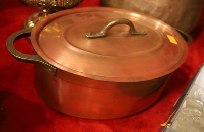 une casserole en cuivre avec une poignée, posée sur une nappe rouge