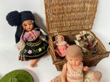 two dolls sitting next to a wicker basket with a doll in it