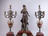 a statue of a woman holding a clock next to three candelabs