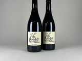two bottles of red wine sitting on top of a white table