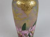 un vase doré sur lequel est peinte une fleur rose