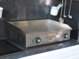 une plaque de cuisson en acier inoxydable dans une cuisine où des casseroles et des ustensiles sont suspendus au mur
