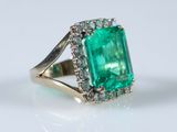 a close up of an emerald and diamond ring on a white surface