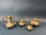 trois théières en métal argenté et une cafetière posées sur une table