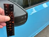a person holding a ruler in front of a blue car