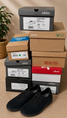 Plusieurs cartons de chaussures sont empilés sur une table, à côté d'une plante en pot.