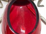 a red glass vase with a silver lid on a white surface