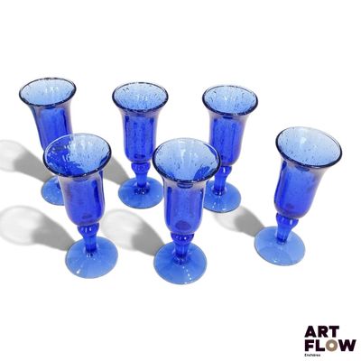 six verres à vin bleus alignés sur une surface blanche