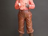 statue d'un garçon portant un chapeau et un pantalon marron, tenant un pistolet
