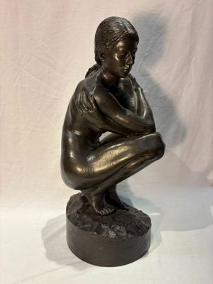 bronze statue of a boy sitting on a rock with his hands on his knees