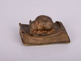 une petite souris en bronze posée sur un livre, sur une surface blanche