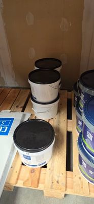 several buckets of paint sitting on a pallet in a room