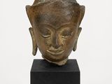 une image représentant une tête de Bouddha en bronze posée sur un socle noir