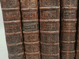six old books are lined up in a row on a white surface