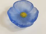 une fleur en verre bleue au cœur jaune, posée sur une surface blanche