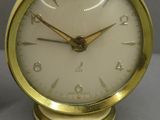 une horloge en or posée sur une table, à côté d'une tasse