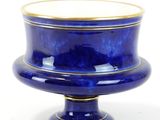 un vase bleu bordé d'or posé sur une surface blanche
