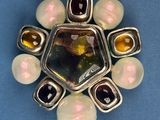 silver and glass broochle with multi colored stones on a blue surface