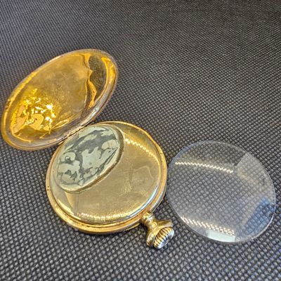 une montre de poche en or posée sur une table, à côté d'une loupe