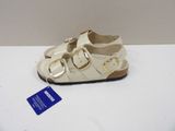 white leather sandals with gold buckles and a tag on a white surface