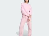 a woman in a pink sweatshirt and sweatpants stands in front of a white background