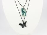 un collier noir et vert orné d'un pendentif en forme d'oiseau, porté par un mannequin blanc