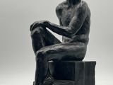 photographie en noir et blanc représentant la statue d'un homme assis sur une caisse