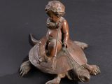 bronze figurine of a boy on a turtle with a fish