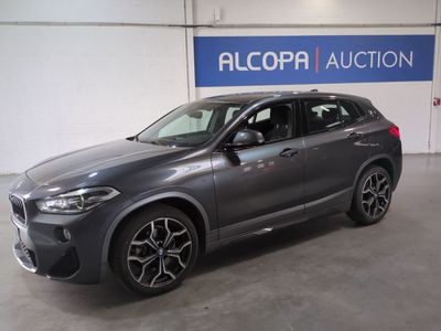 un SUV BMW gris garé devant un panneau indiquant « Alcopa Auction »