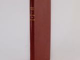 an old book with a red cover sitting on top of a white surface