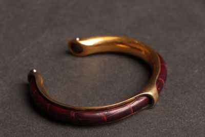 une image représentant un bracelet rouge et doré posé sur un fond noir
