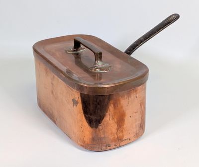 une petite casserole en cuivre avec une poignée, posée sur une surface blanche