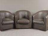 trois fauteuils en cuir marron placés les uns à côté des autres sur un sol blanc