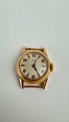 une montre en or avec un cadran blanc posée sur une surface blanche
