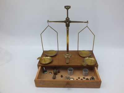 une vieille balance à fléaux avec un plateau rempli de pièces et une paire de lunettes