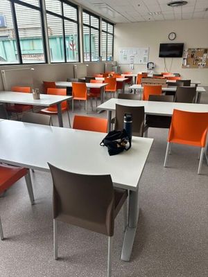 Il y a de nombreuses tables et chaises dans cette salle de classe, avec une horloge accrochée au mur.