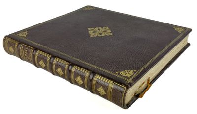 un vieux livre marron avec des bordures dorées posé sur une surface blanche