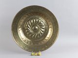 une assiette en or posée sur un socle, sur fond blanc