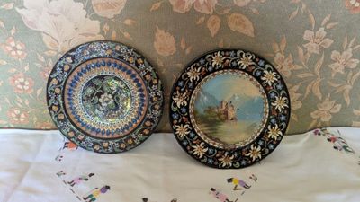 two decorative plates sitting on a bed with a floral wallpaper