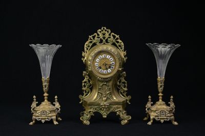 une horloge dorée et trois vases en verre sur fond noir