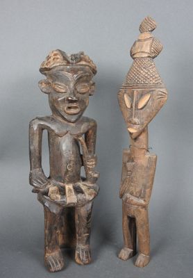 deux statues en bois représentant des personnes debout l'une à côté de l'autre sur une surface grise