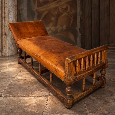 un banc en bois avec une assise en cuir marron, placé face à un mur