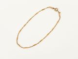 a gold chain bracelet with a small bead on a white background