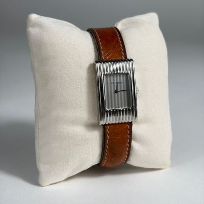 un oreiller blanc entouré d'une sangle marron, avec une montre posée dessus