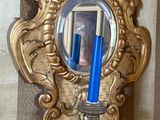 un miroir doré accroché au mur, dans lequel se reflète une bougie bleue