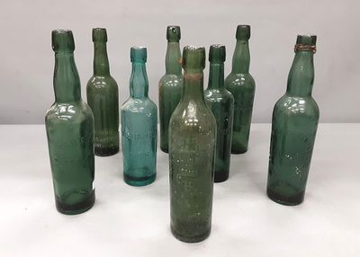 Plusieurs bouteilles en verre vert sont alignées sur une surface blanche
