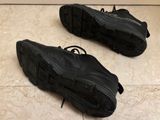 pair of black sneakers with laces on the soles on a tiled floor