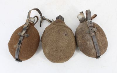 three old, rusty, and worn flasks sitting on a white surface