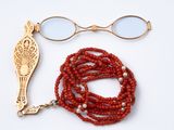 un collier de perles rouges et une paire de lunettes posés sur une surface blanche