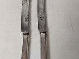 pair of silverware knives on a white table with a white background